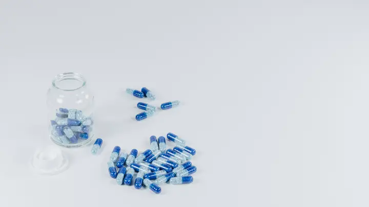 Blau-weiße Kapseln und ein offenes Glas auf weißem Untergrund