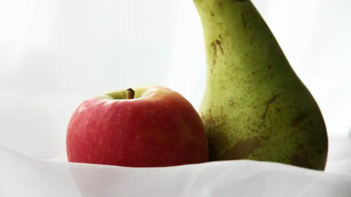 Ein roter Apfel und eine grüne Birne vor hellem Hintergrund