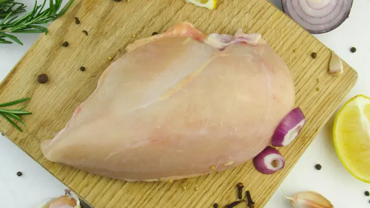 Rohe Hähnchenbrust auf einem Holzbrett mit Zitrone, Knoblauch und Kräutern