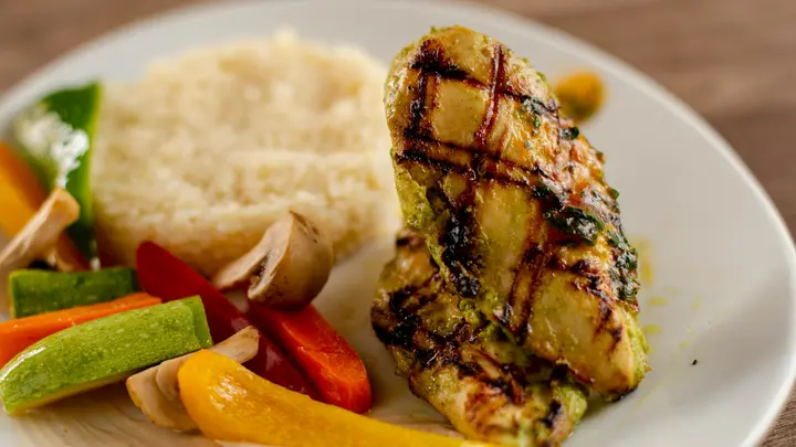 Gegrillte Hähnchenbrust mit Couscous, Paprika, Zucchini und Champignons auf einem hellen Teller