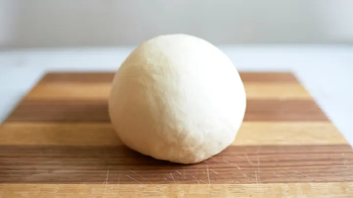 Eine Kugel heller Hefeteig auf einem Holzbrett vor hellem Hintergrund