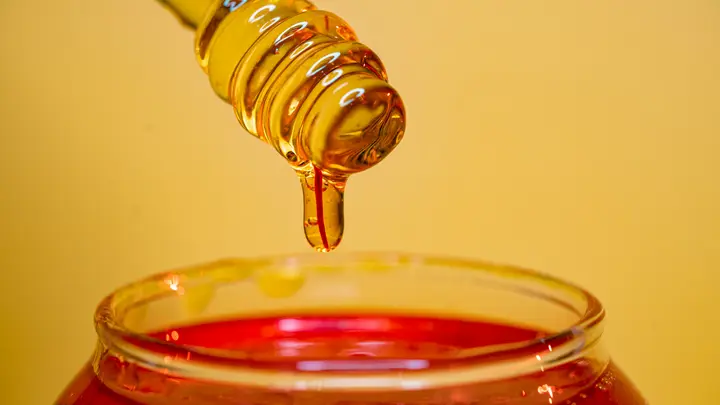 Goldener Honig tropft von einem Honiglöffel in ein Glas