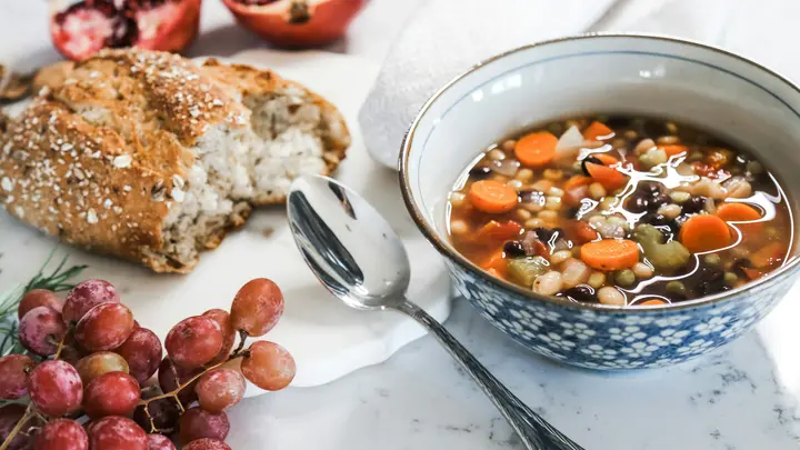 Bohnensuppe mit Karotten in einer blau gemusterten Schale, daneben Brot, Trauben und Granatapfel