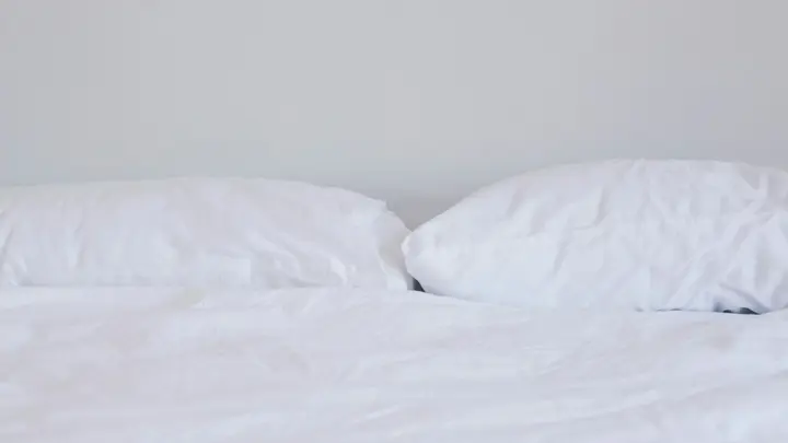 Frisch bezogenes Bett mit weißer Bettwäsche und zwei Kissen vor einer hellen Wand