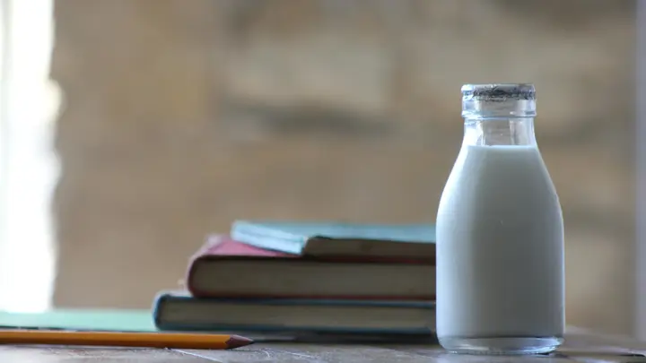 Eine Glasflasche Milch auf einem Holztisch neben einem Stapel Bücher