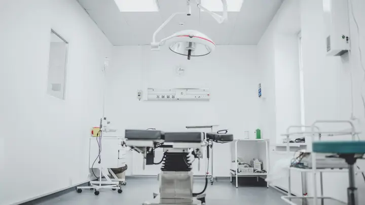 Heller, leerer Operationssaal mit OP-Tisch, Deckenleuchte und medizinischen Geräten