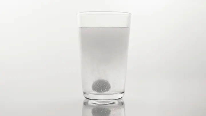 Eine Brausetablette löst sich in einem Glas Wasser vor hellem Hintergrund auf