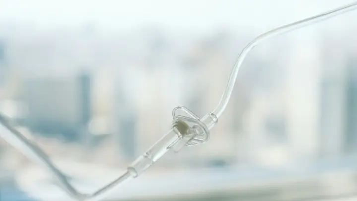 Durchsichtiger Infusionsschlauch mit Anschlussstück vor einem hellen, unscharfen Fenster