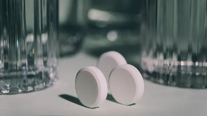 Drei weiße Tabletten zwischen Wassergläsern auf salbeigrünem Untergrund