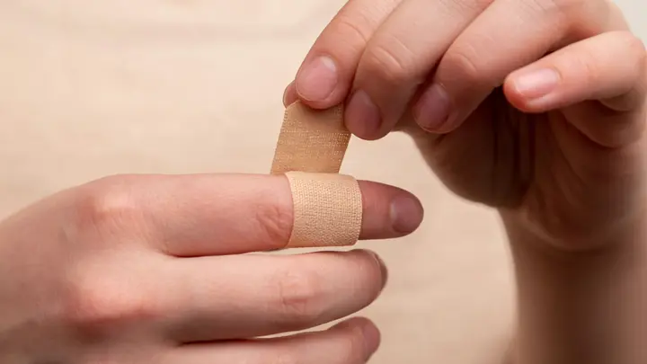 Hände kleben ein hautfarbenes Pflaster um einen Finger