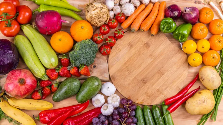 Buntes Obst und Gemüse rund um ein rundes Holzbrett