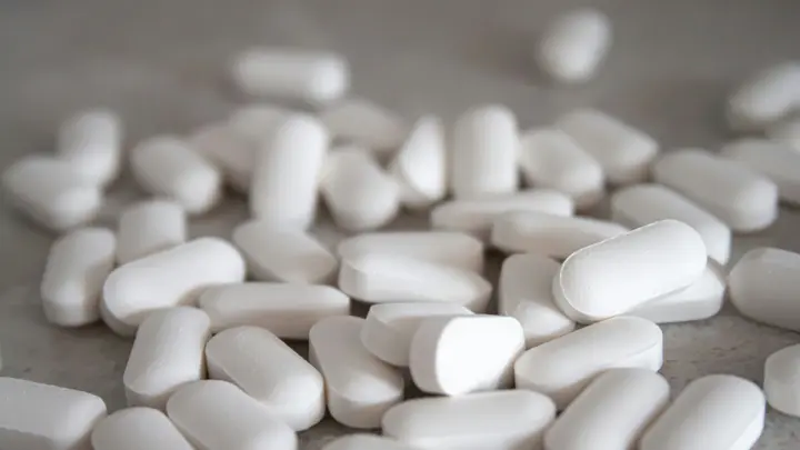 Viele weiße längliche Tabletten auf einer grauen Steinoberfläche