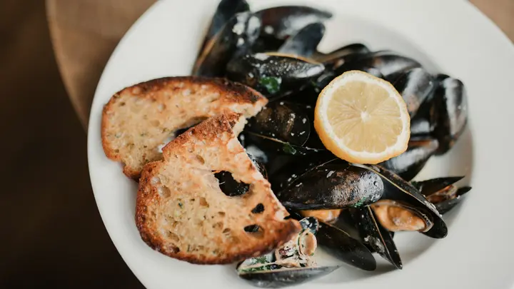 Gekochte Miesmuscheln mit einer Zitronenscheibe und geröstetem Brot auf einem weißen Teller